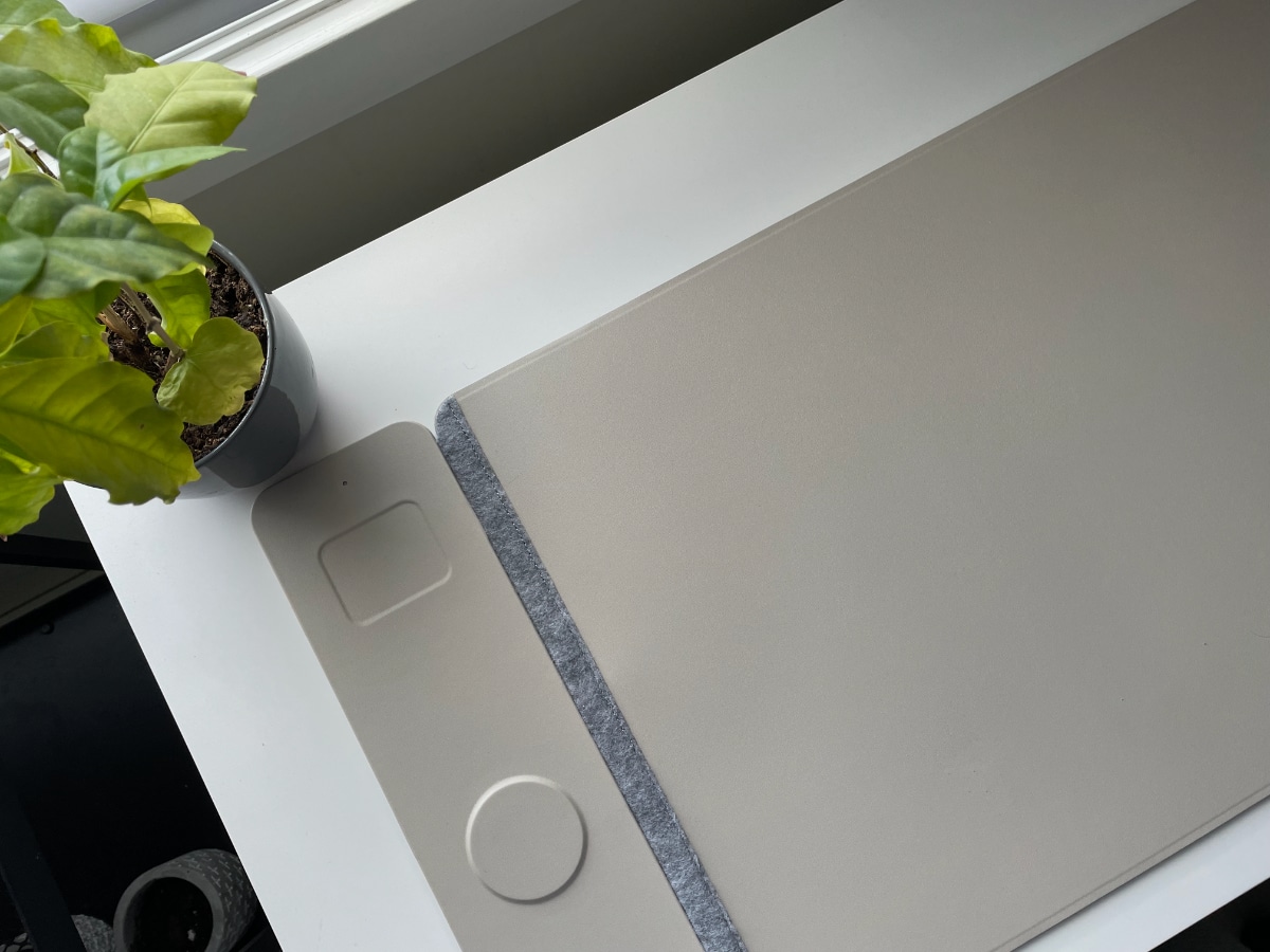 A white desk with a plant, and a computer mat that has two wireless charging areas.