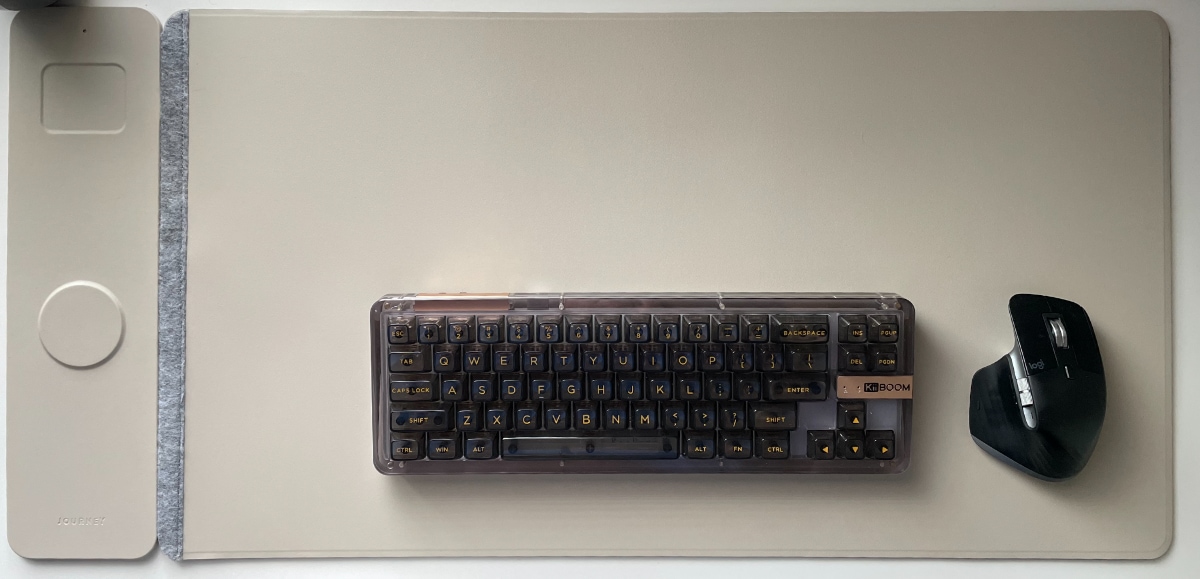 A photo of a desk with a keyboard and a mouse on a computer mat. The mat has a white circle and a white rectangle that are wireless charging areas. The circle has a puck on it and the rectangle is empty.