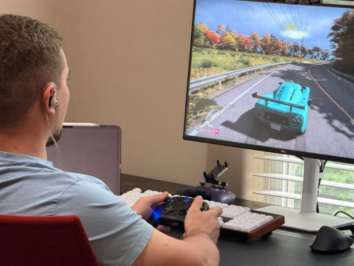 User wearing ATK Horizon earphones while playing a racing game with a controller at a desktop gaming setup. User wearing ATK Horizon earphones while playing a racing game with a controller at a desktop gaming setup.