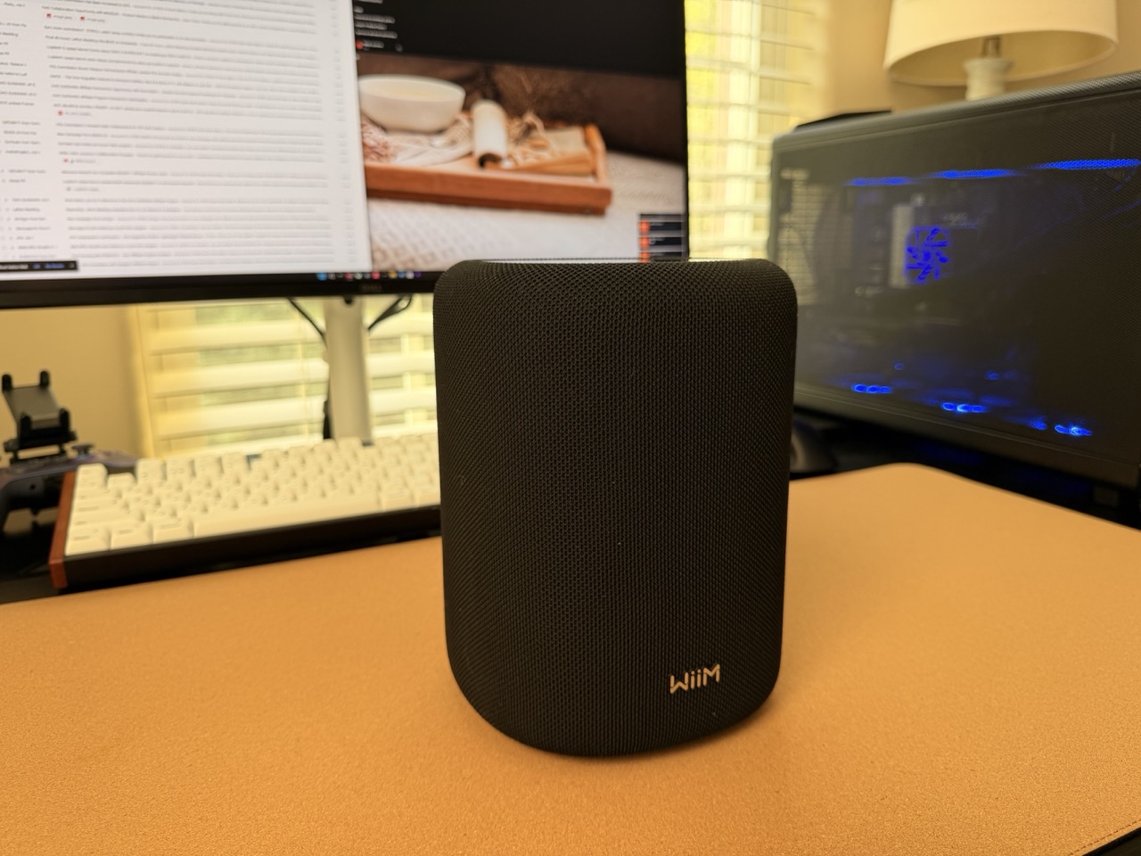 WiiM Sound Lite wireless WiiM Sound Lite wireless smart speaker in black placed on an office desk, with a desktop PC and monitor in the background, highlighting its compact size in a real-world workspace.
